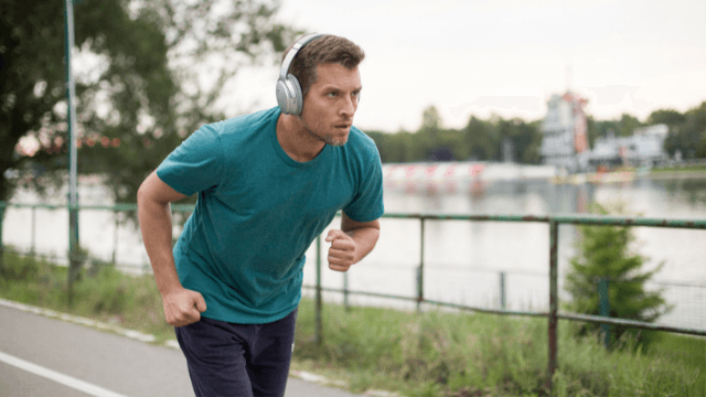 Man in a teal shirt and headphones running hard on a path beside a river